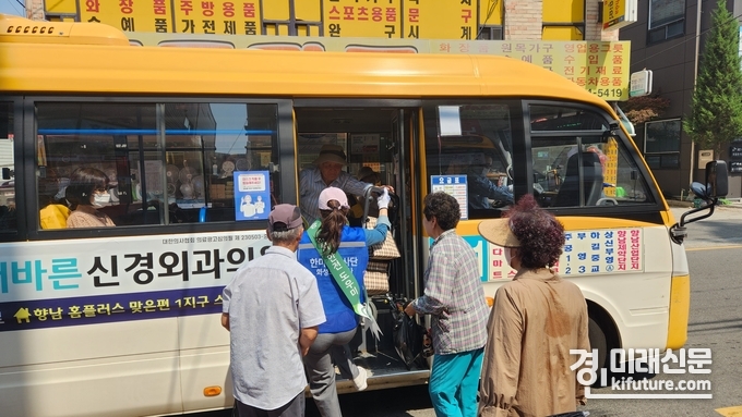 발안 만세시장 앞 정류장에서 승하차 안전도우미 활동을 수행한 HU공사 임직원이 어르신의 무거운 짐을 들어주고 있다. <사진=화성도시공사>